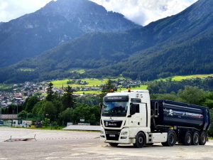 AE LKW steht auf einem Parkplatz, im Hintergrund sind die Alpen zu sehen.